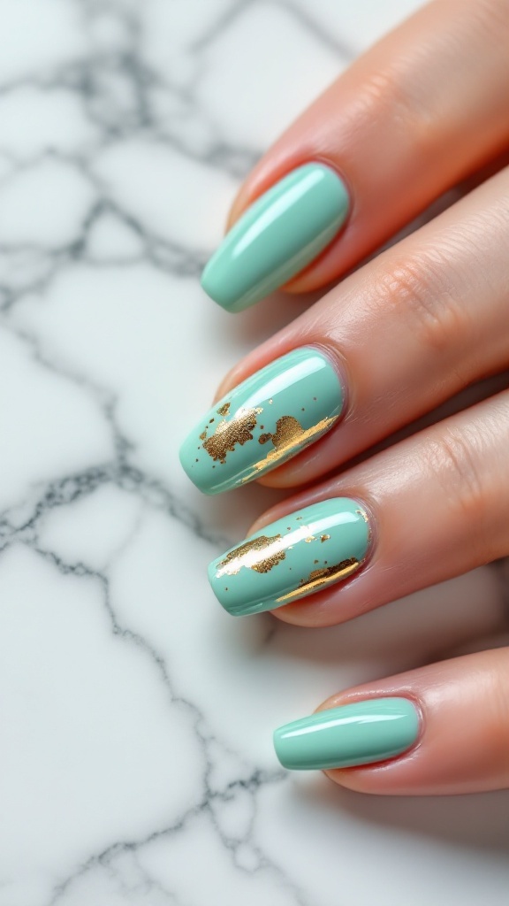 Mint green nails with gold accents on a marble surface.